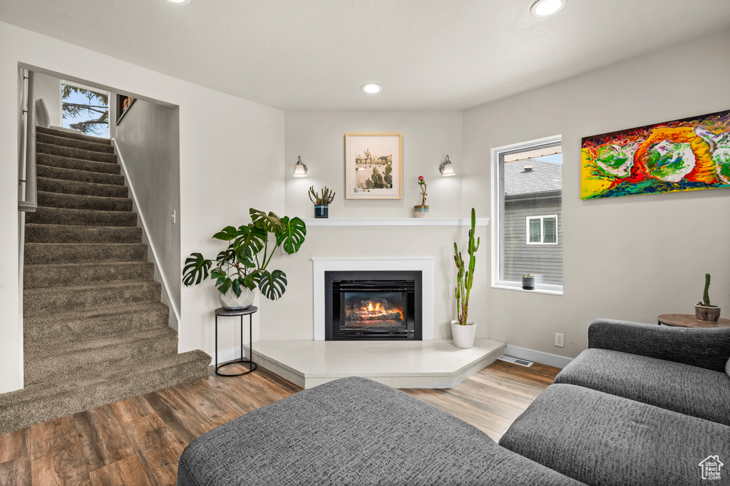 Living area featuring a glass covered fireplace, wood finished floors, stairs, and recessed lighting