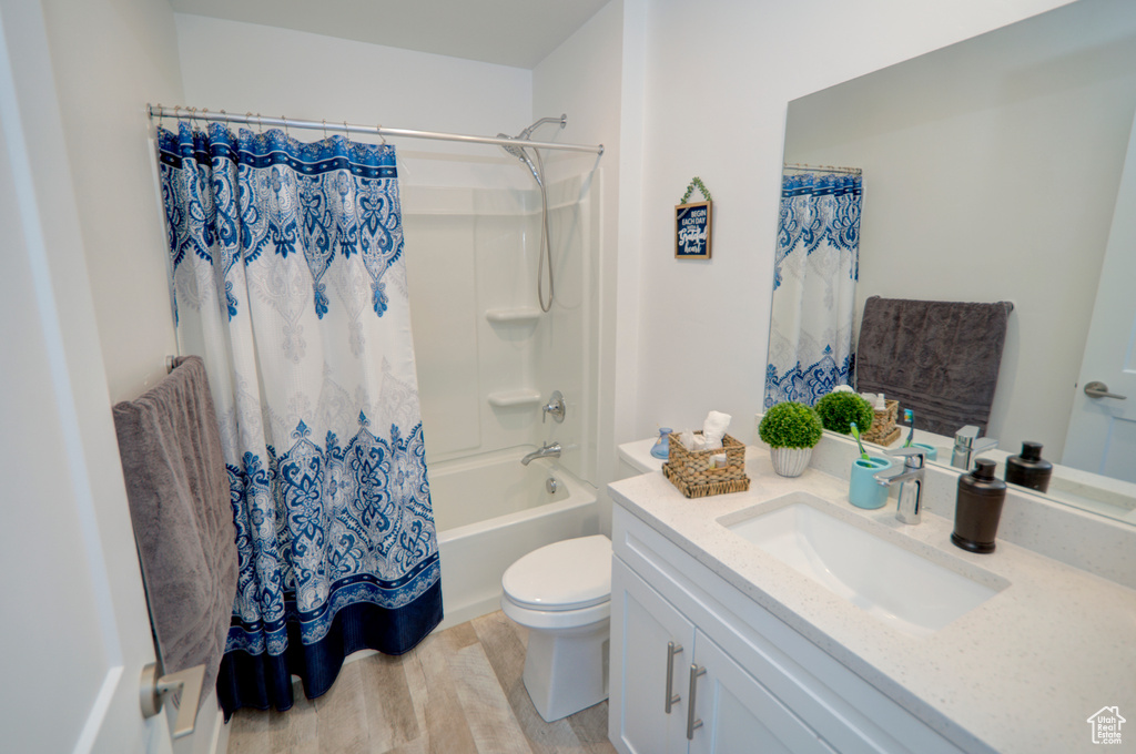 Bathroom with toilet, shower / tub combo with curtain, vanity, and wood finished floors
