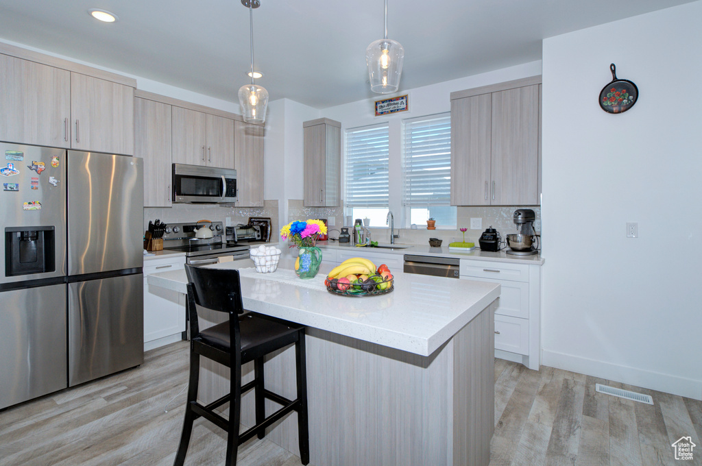 Kitchen featuring stainless steel appliances, a center island, tasteful backsplash, light wood-type flooring, and light countertops