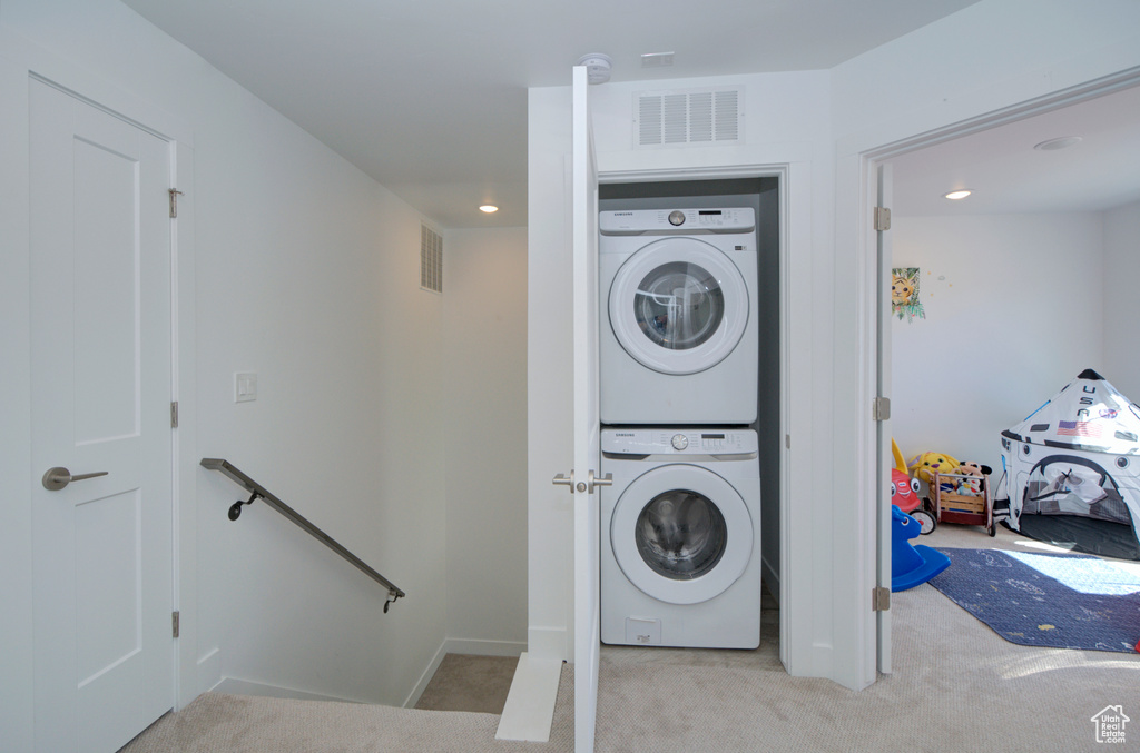 Laundry room with carpet, visible vents, stacked washing maching and dryer, and laundry area