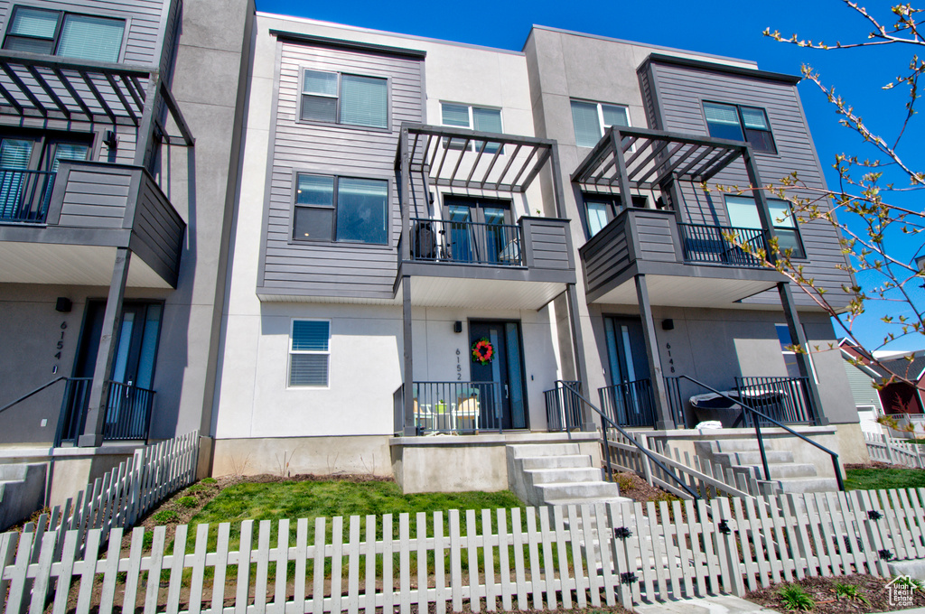 Townhome / multi-family property with a balcony, a fenced front yard, and stucco siding