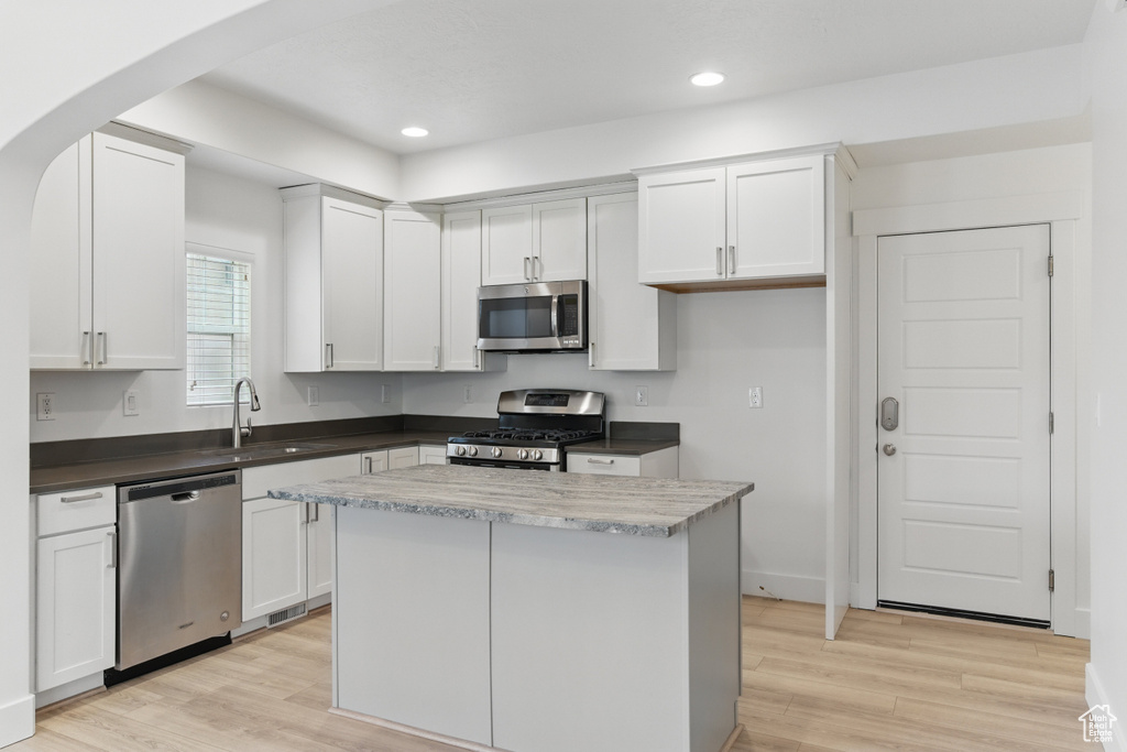 Kitchen featuring white cabinets, light wood finished floors, a sink, arched walkways, and appliances with stainless steel finishes