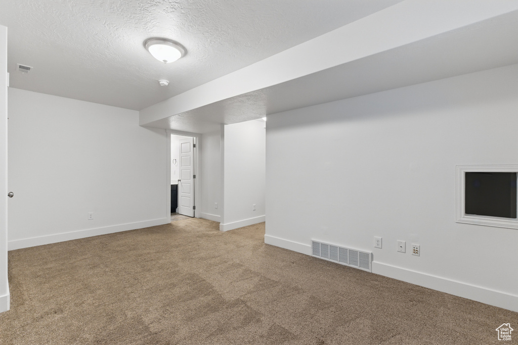 Finished basement featuring light carpet, a textured ceiling, visible vents, and baseboards