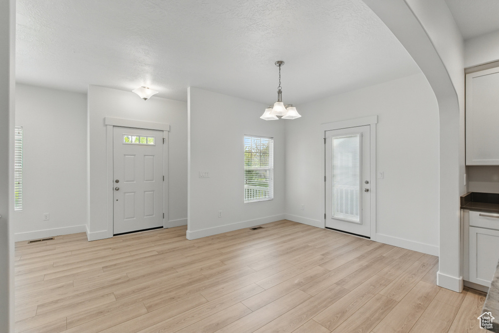 Foyer entrance featuring arched walkways, light wood-style floors, visible vents, and baseboards