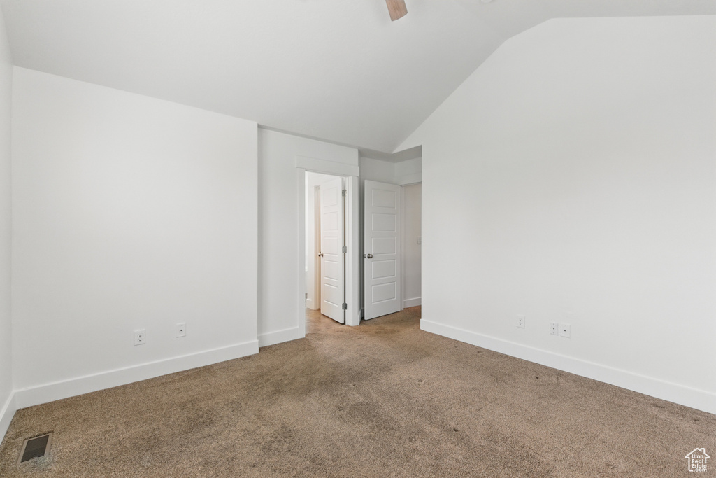 Carpeted spare room featuring lofted ceiling, a ceiling fan, visible vents, and baseboards