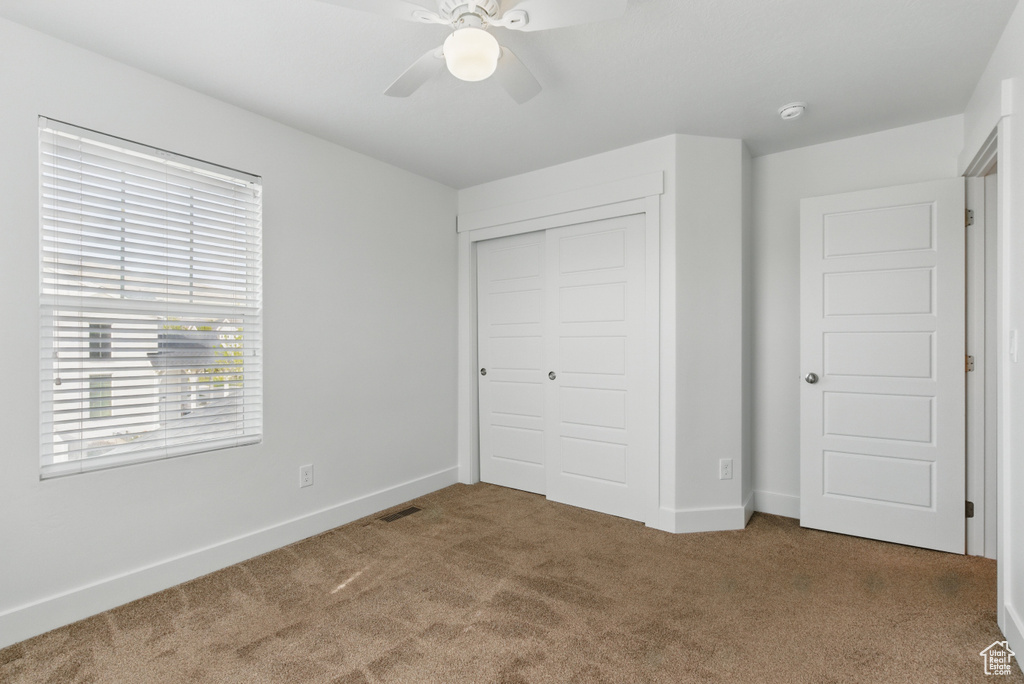 Unfurnished bedroom featuring carpet floors, multiple windows, visible vents, and a closet