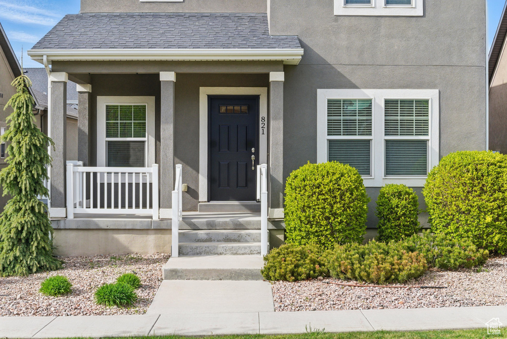 Property entrance featuring a porch, stucco siding, and a shingled roof