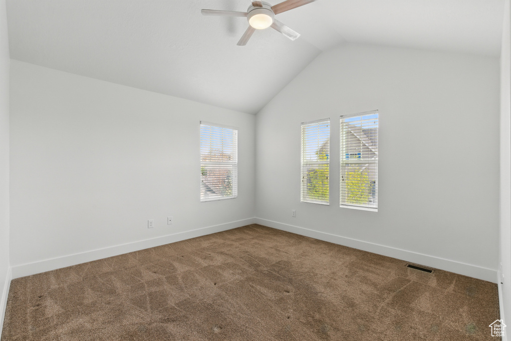 Empty room with carpet floors, visible vents, lofted ceiling, and a ceiling fan