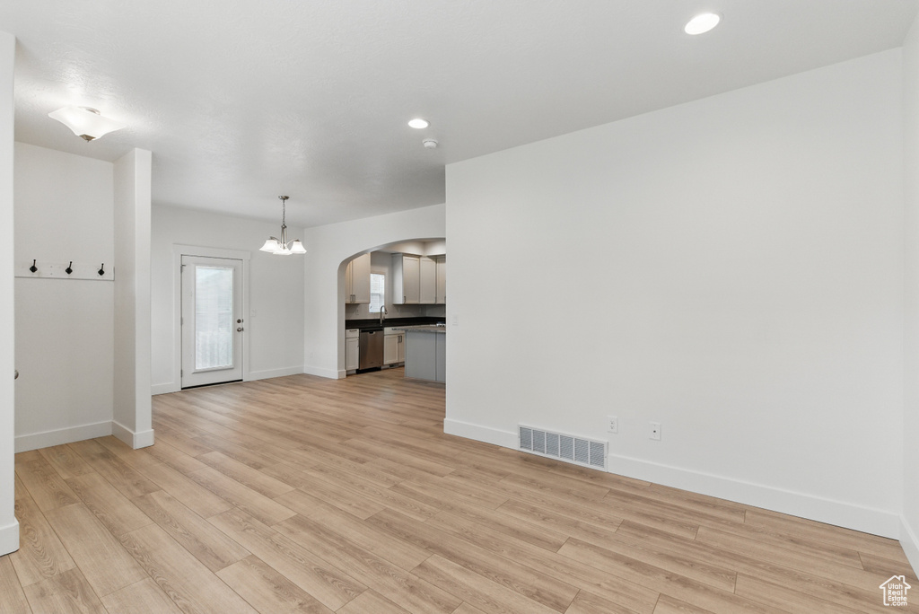Unfurnished living room featuring light wood finished floors, baseboards, visible vents, and arched walkways