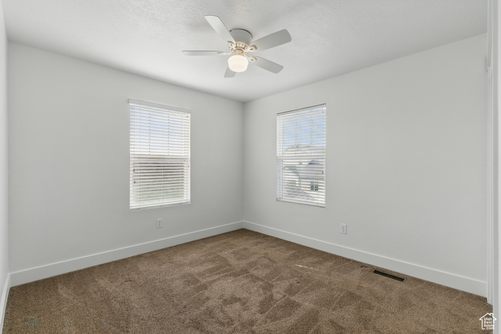 Empty room featuring carpet floors, visible vents, a ceiling fan, and baseboards