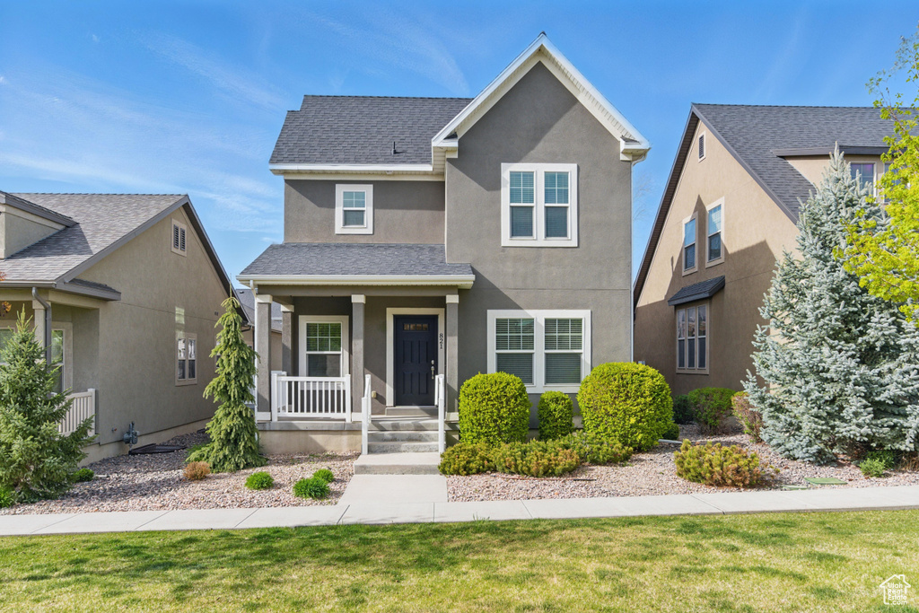 Traditional-style home featuring a shingled roof, covered porch, a front yard, and stucco siding