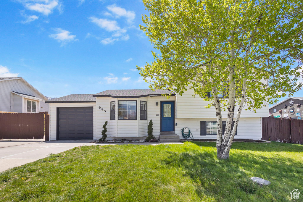 Split level home with a front lawn, concrete driveway, fence, a garage, and entry steps