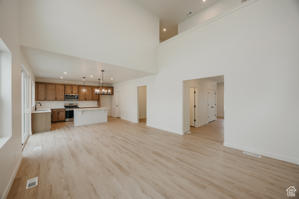 Unfurnished living room with light wood-type flooring, an inviting chandelier, visible vents, and a sink