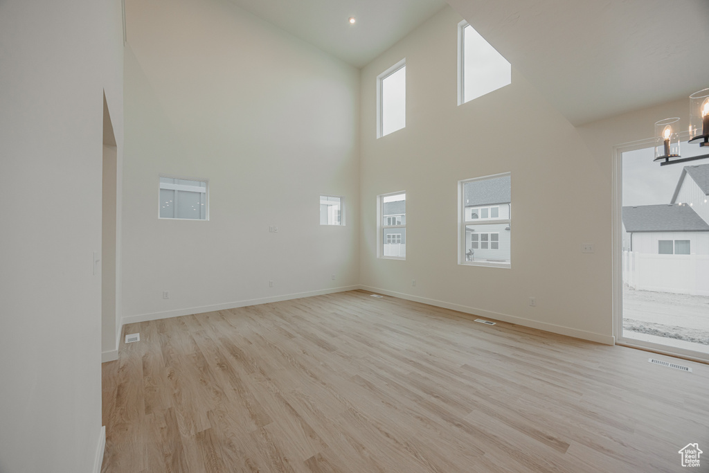 Unfurnished living room featuring a chandelier, light wood-style floors, visible vents, and high vaulted ceiling