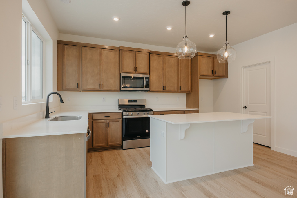 Kitchen with a sink, light wood-type flooring, brown cabinets, a kitchen island, and appliances with stainless steel finishes