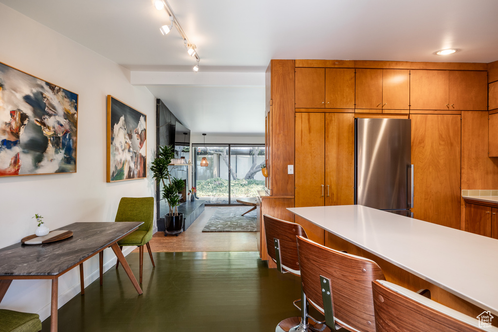 Kitchen with lofted ceiling, light countertops, track lighting, freestanding refrigerator, and brown cabinetry