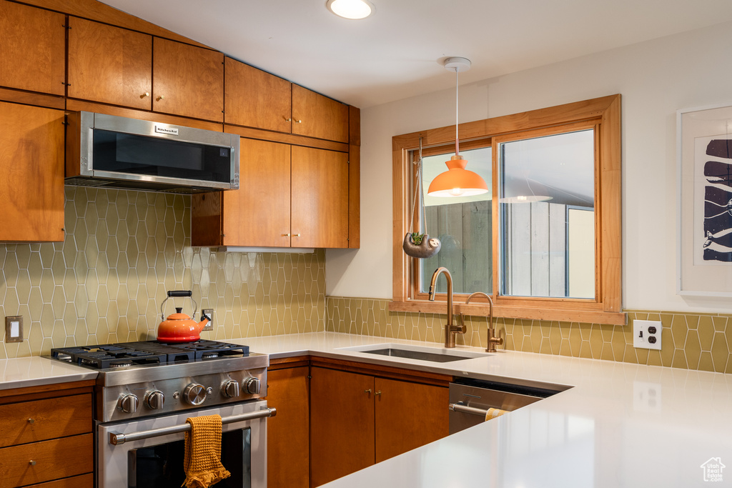 Kitchen featuring decorative backsplash, brown cabinetry, a sink, and appliances with stainless steel finishes