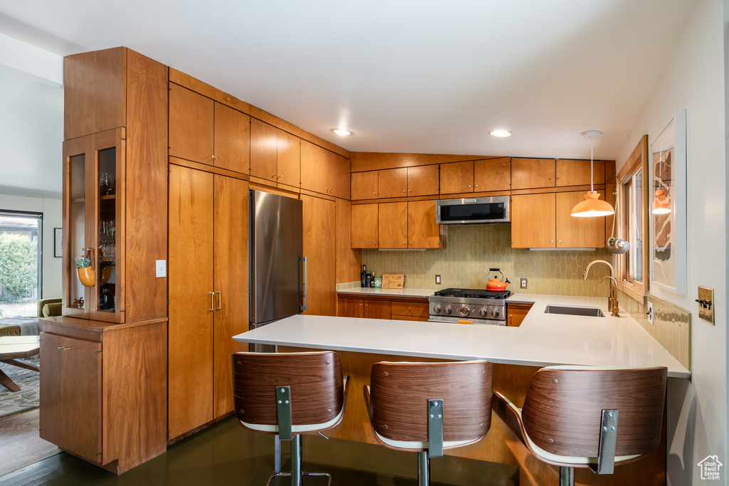 Kitchen with a peninsula, a sink, brown cabinets, light countertops, and appliances with stainless steel finishes