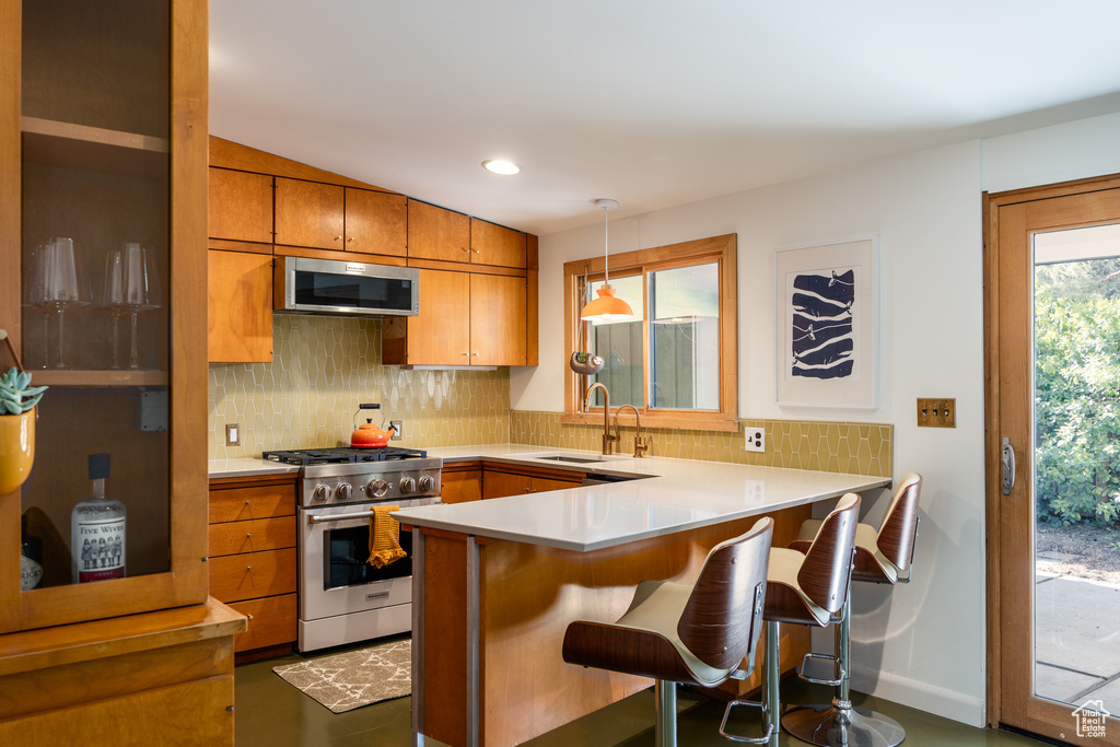 Kitchen with backsplash, a peninsula, appliances with stainless steel finishes, and a sink