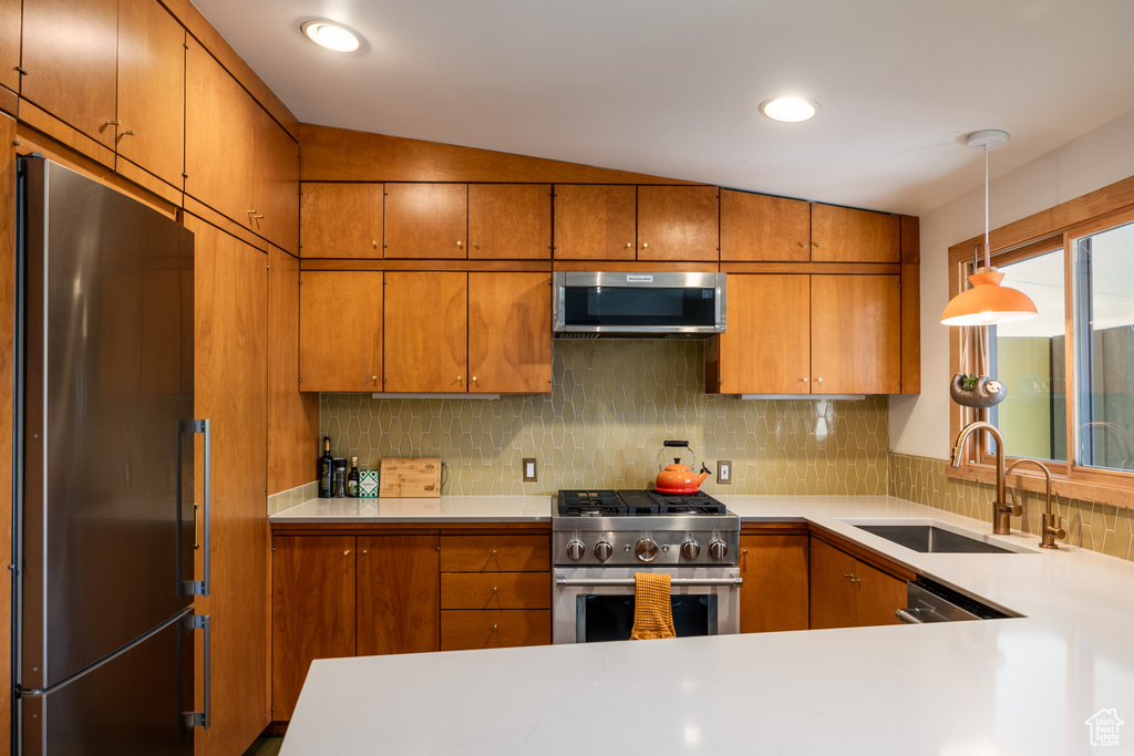 Kitchen with brown cabinetry, a sink, appliances with stainless steel finishes, and tasteful backsplash