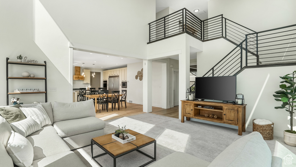 Living area with light wood finished floors, a high ceiling, recessed lighting, and stairway