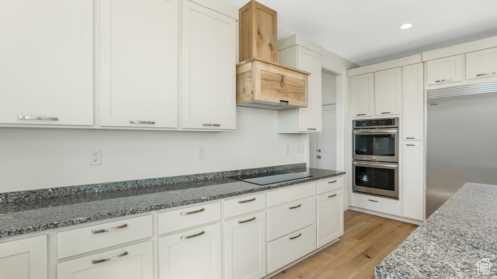Kitchen with light wood-type flooring, custom range hood, white cabinetry, and appliances with stainless steel finishes
