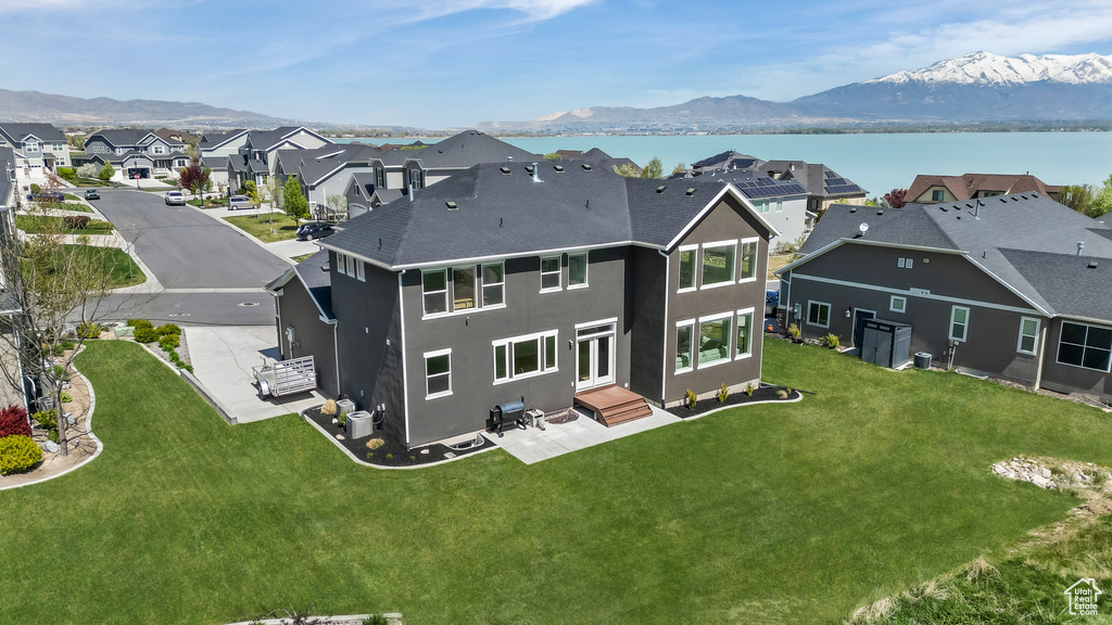 Back of house with a residential view, a water and mountain view, a patio area, a lawn, and stucco siding