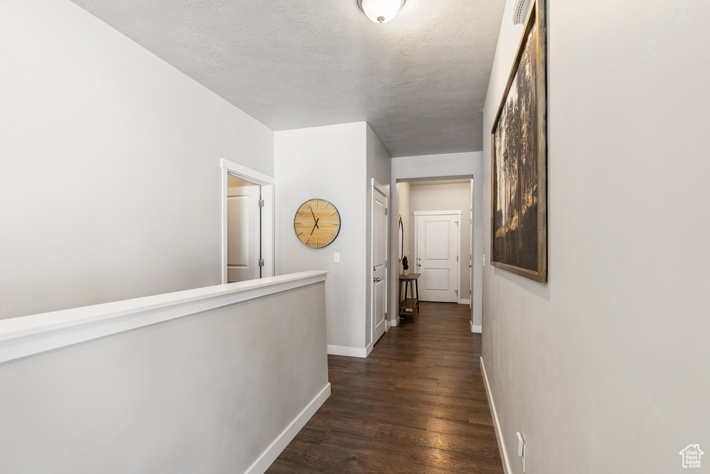 Hall with baseboards, dark wood-type flooring, and a textured ceiling