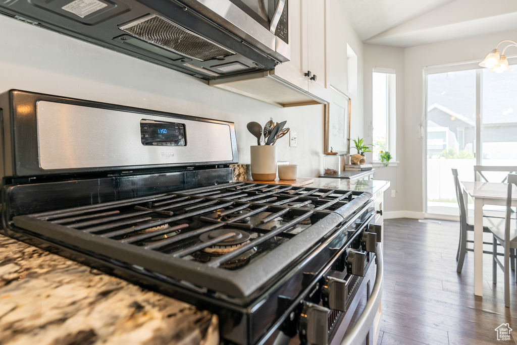 Kitchen with stainless steel appliances, white cabinets, dark wood-style flooring, baseboards, and vaulted ceiling