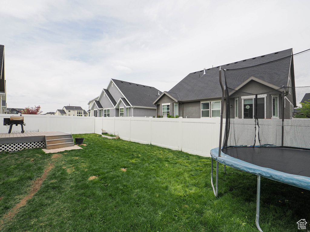 View of yard featuring a fenced backyard, a wooden deck, and a trampoline