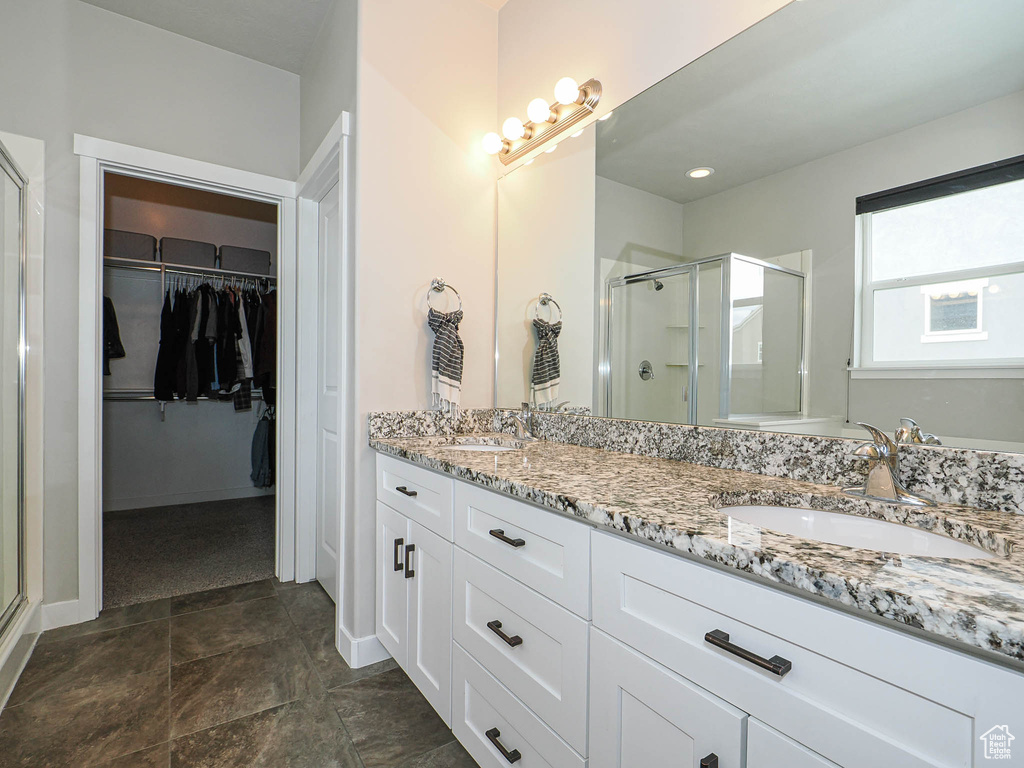 Full bathroom with a walk in closet, double vanity, a shower stall, and a sink