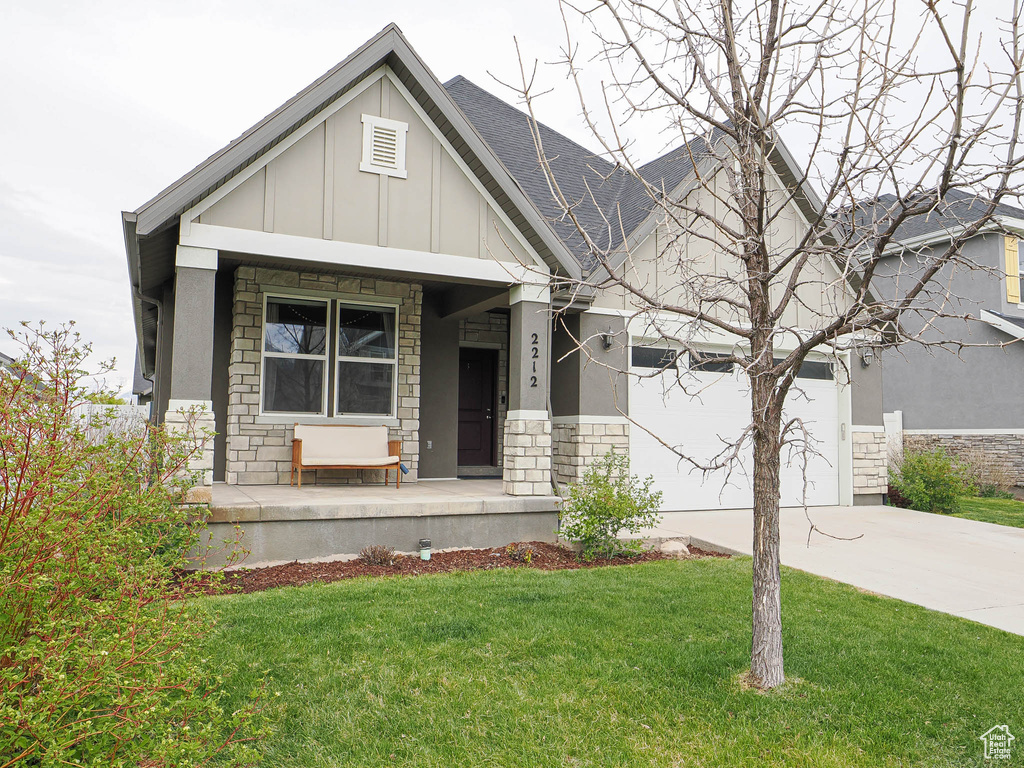 Craftsman inspired home featuring driveway, stone siding, covered porch, board and batten siding, and a front yard