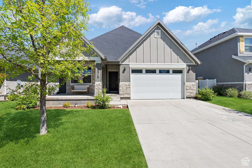 Craftsman inspired home featuring stone siding, board and batten siding, a garage, and a front lawn