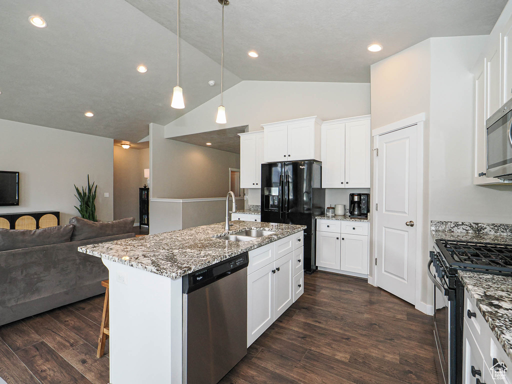 Kitchen featuring vaulted ceiling, a sink, light stone countertops, appliances with stainless steel finishes, and open floor plan