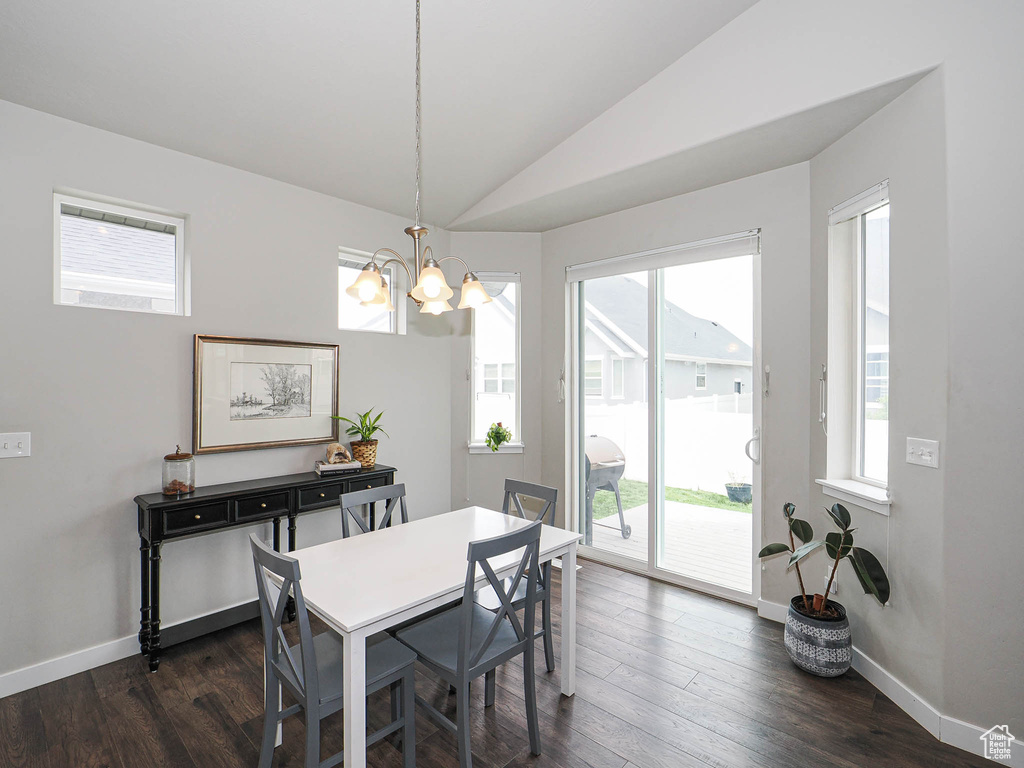 Dining area featuring lofted ceiling, a notable chandelier, dark wood-style floors, and a wealth of natural light