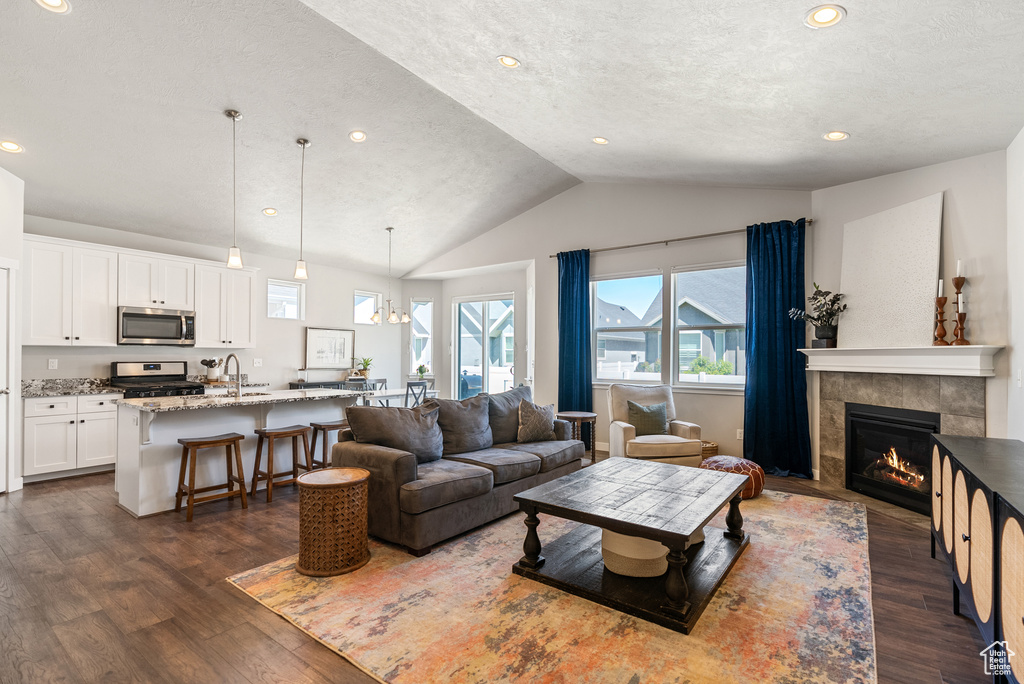 Living area with lofted ceiling, dark wood-style floors, a tile fireplace, recessed lighting, and a textured ceiling