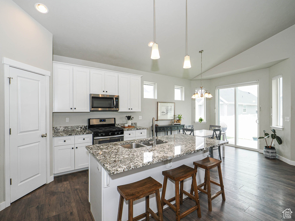 Kitchen with light stone counters, a kitchen breakfast bar, a sink, stainless steel appliances, and lofted ceiling