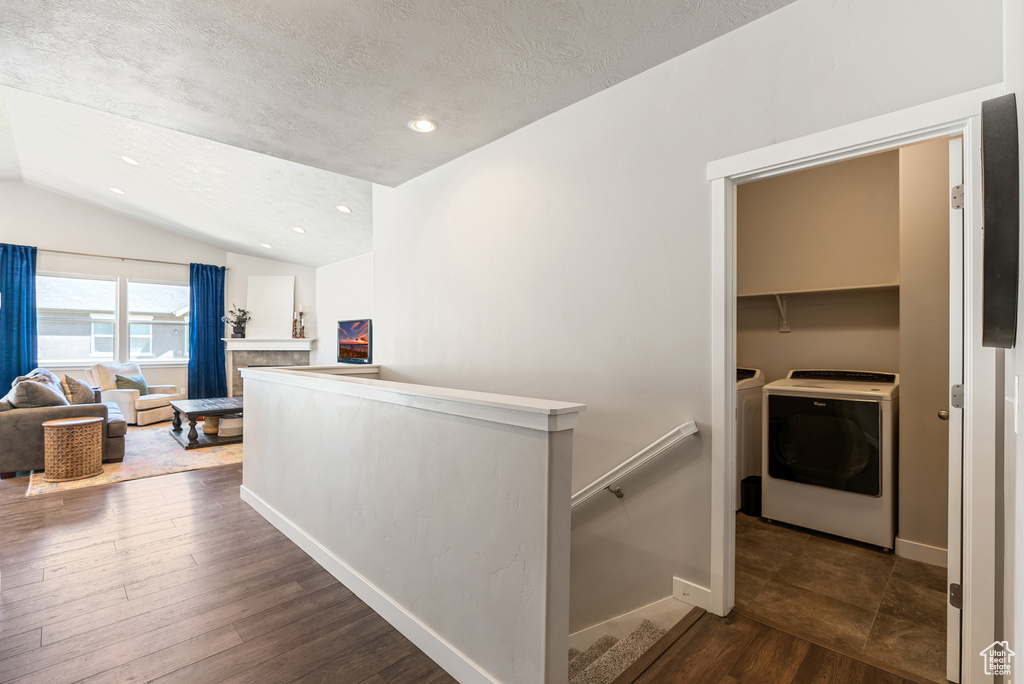 Corridor with an upstairs landing, vaulted ceiling, washing machine and dryer, a textured ceiling, and dark wood finished floors