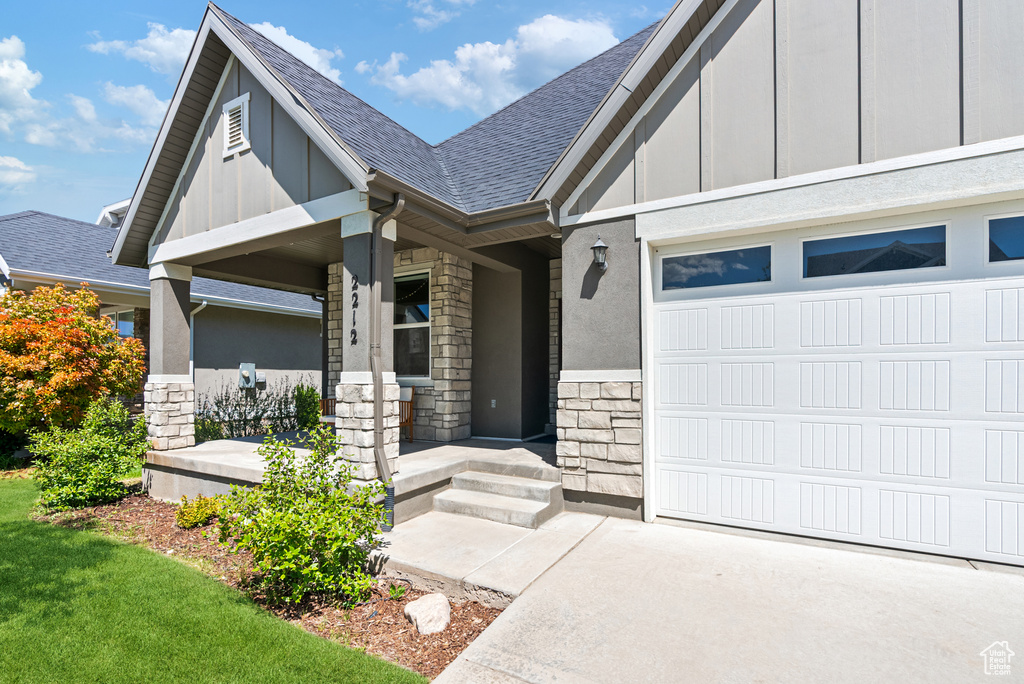 Doorway to property with a porch, stone siding, a shingled roof, an attached garage, and board and batten siding