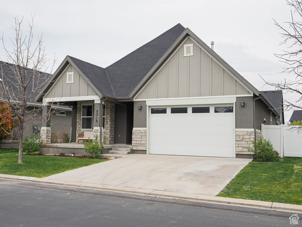 Craftsman inspired home featuring concrete driveway, board and batten siding, stone siding, a front yard, and a garage