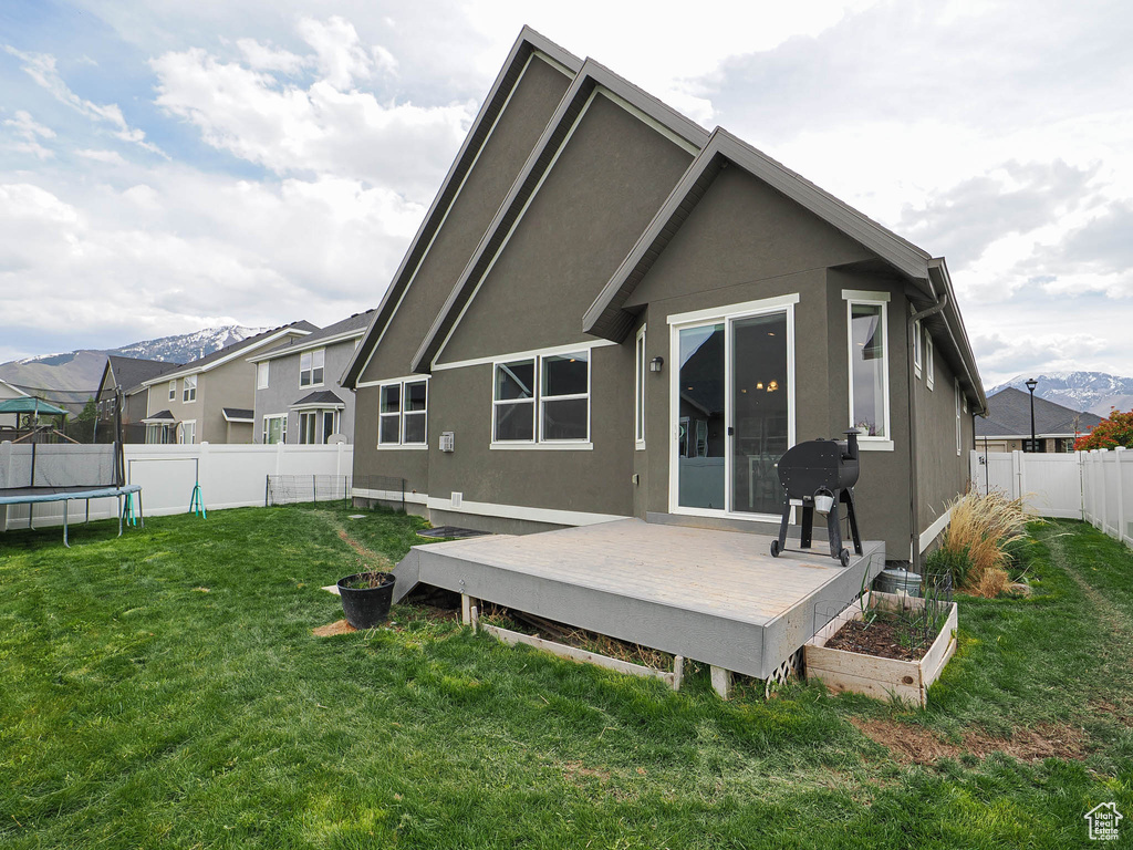 Back of property with a fenced backyard, a wooden deck, a trampoline, a yard, and stucco siding