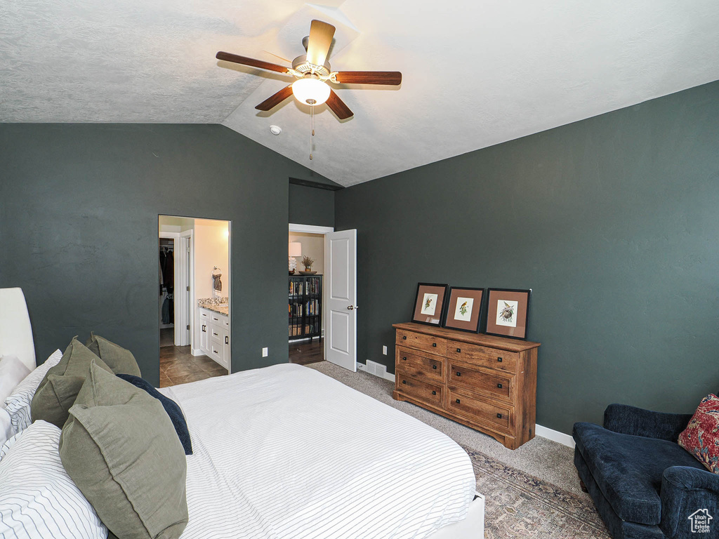 Carpeted bedroom featuring ensuite bath, vaulted ceiling, baseboards, and a ceiling fan