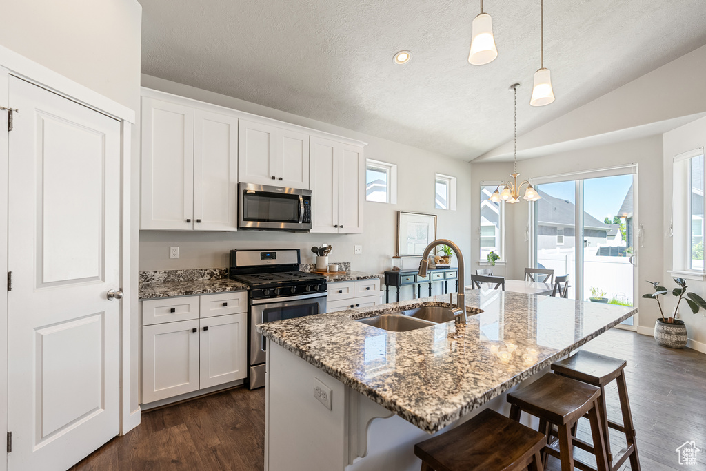 Kitchen featuring stainless steel appliances, a sink, a chandelier, a breakfast bar area, and light stone counters