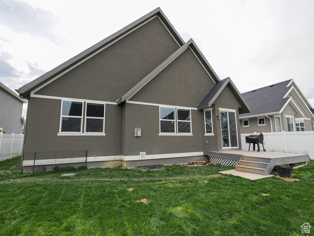 Rear view of property with a wooden deck, stucco siding, a lawn, and fence