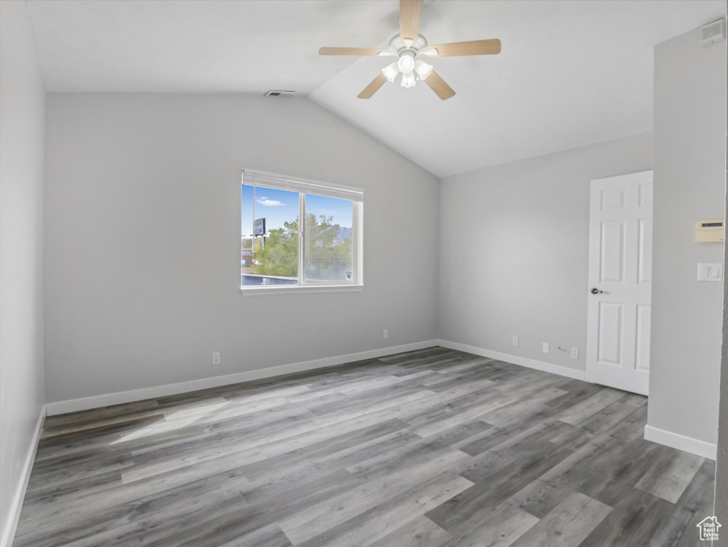 Unfurnished room featuring vaulted ceiling, baseboards, visible vents, wood finished floors, and ceiling fan