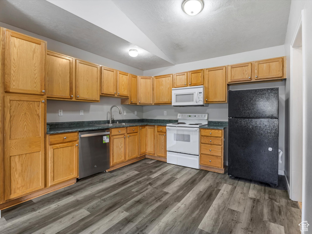 Kitchen with a sink, dark countertops, vaulted ceiling, white appliances, and dark wood-type flooring