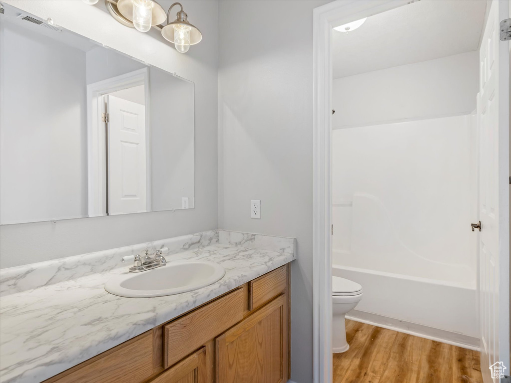 Bathroom with toilet, bathtub / shower combination, visible vents, wood finished floors, and vanity