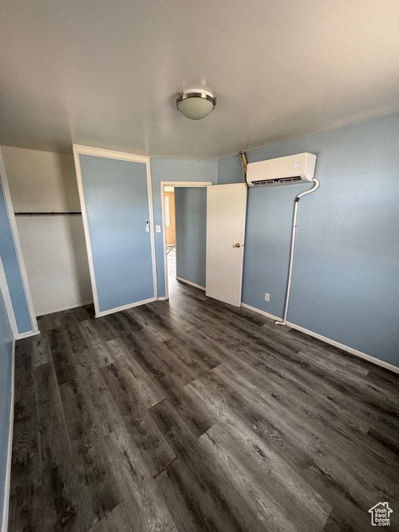Unfurnished bedroom with a wall mounted air conditioner, baseboards, and dark wood-type flooring