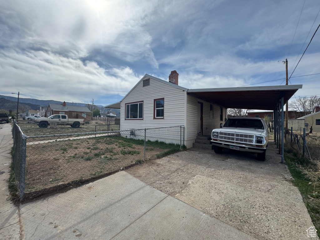 View of side of property featuring fence private yard, driveway, a chimney, and a carport