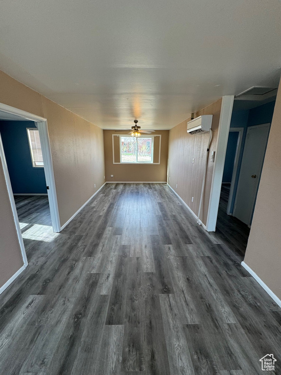Interior space with baseboards, a ceiling fan, a wall unit AC, and dark wood-style flooring